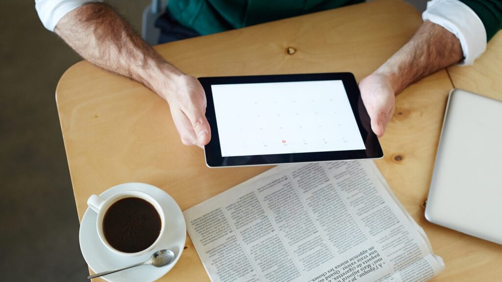 Fontes citadas pela IA: pessoa lendo notícias em um tablet ao lado de um jornal impresso