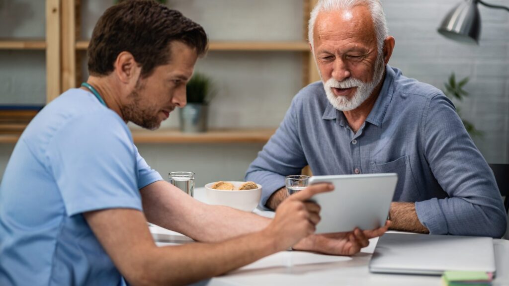 SEO para clínicas e médicos: foto de um profissional de saúde de uniforme azul e um paciente idoso olhando juntos um tablet numa mesa
