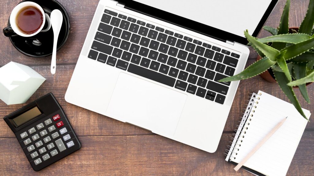 Quanto cobrar por produção de conteúdo: notebook, calculadora, caderno e café sobre uma mesa de madeira