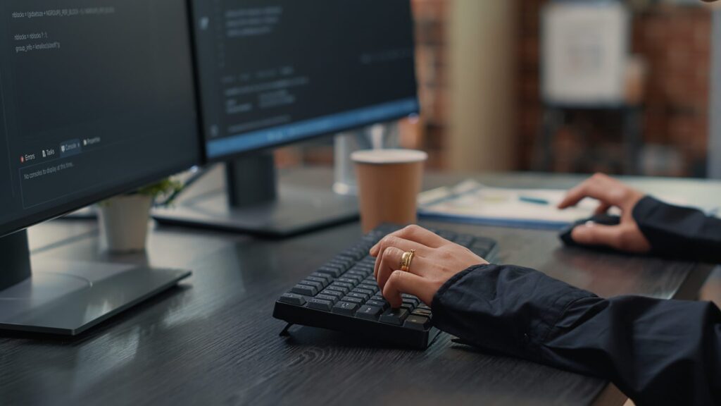 Angular SEO: mãos digitam código diante de dois monitores com a interface de programação