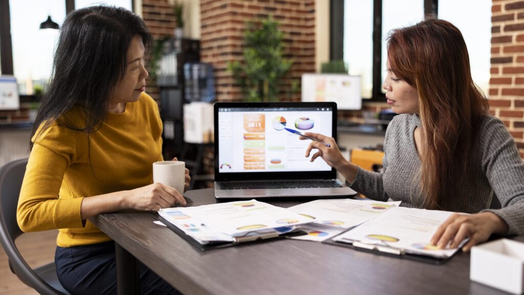 White label GEO services: two professionals reviewing a report with charts on a laptop and on paper at an office desk